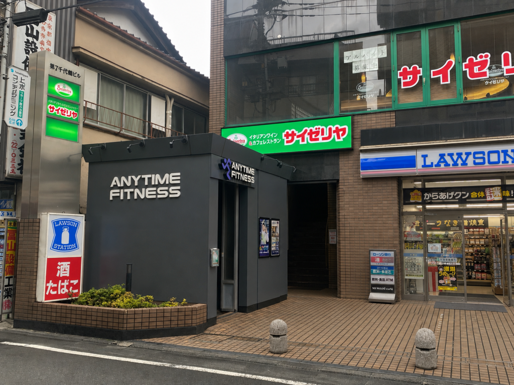 The basement entrance of Anytime Fitness Kokubunji ― a black facade beneath a Saizeriya