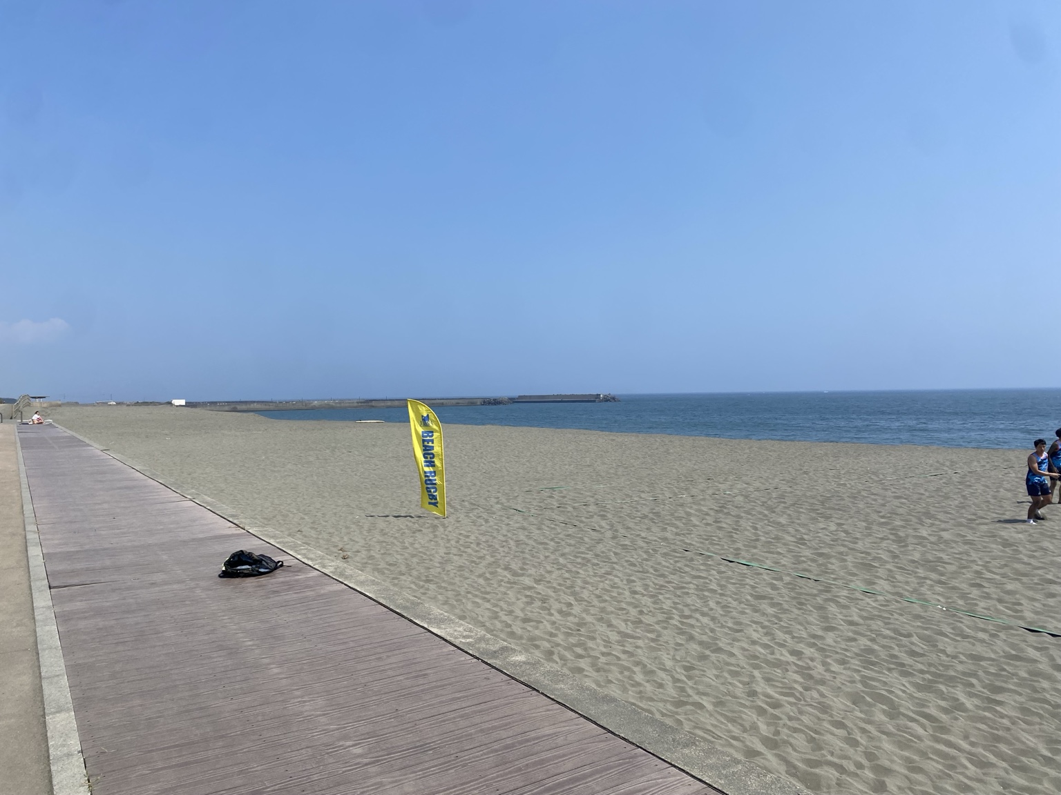 ひらつかビーチパークの砂浜に立つビーチラグビーの旗と選手たち