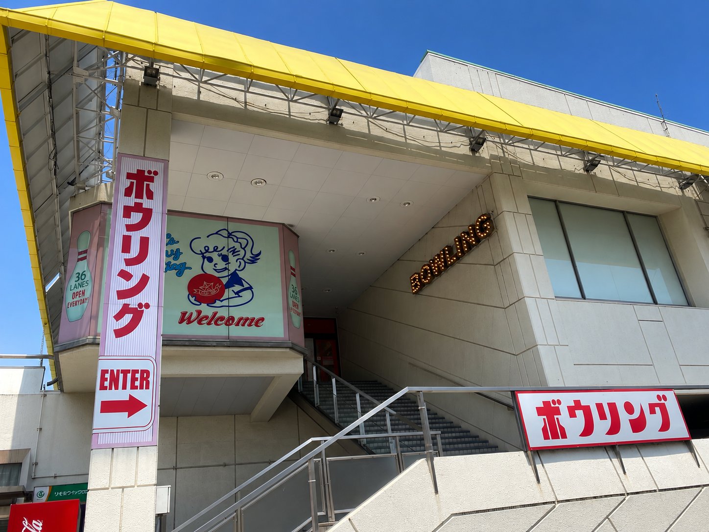 スポルト八景ボウルの入口。黄色い庇と「ボウリング」の看板、エニタイムはこの建物1階