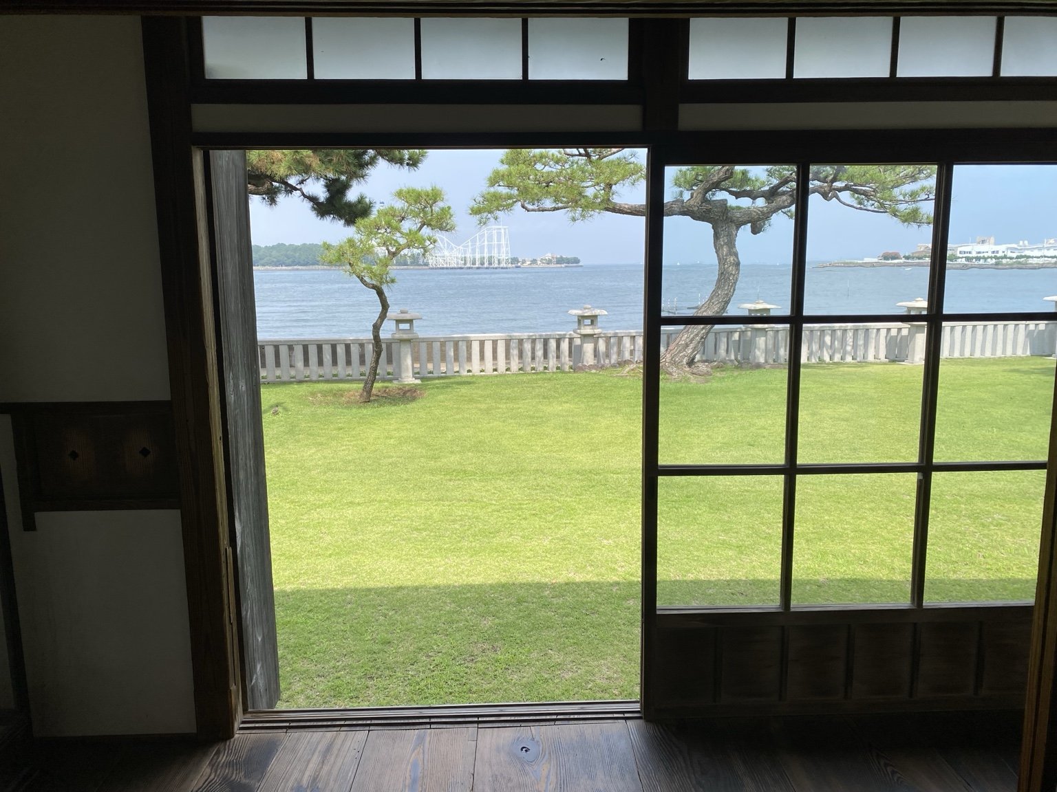 座敷の開口部から芝生の庭と海を望む。石灯籠と松が海との間に並ぶ