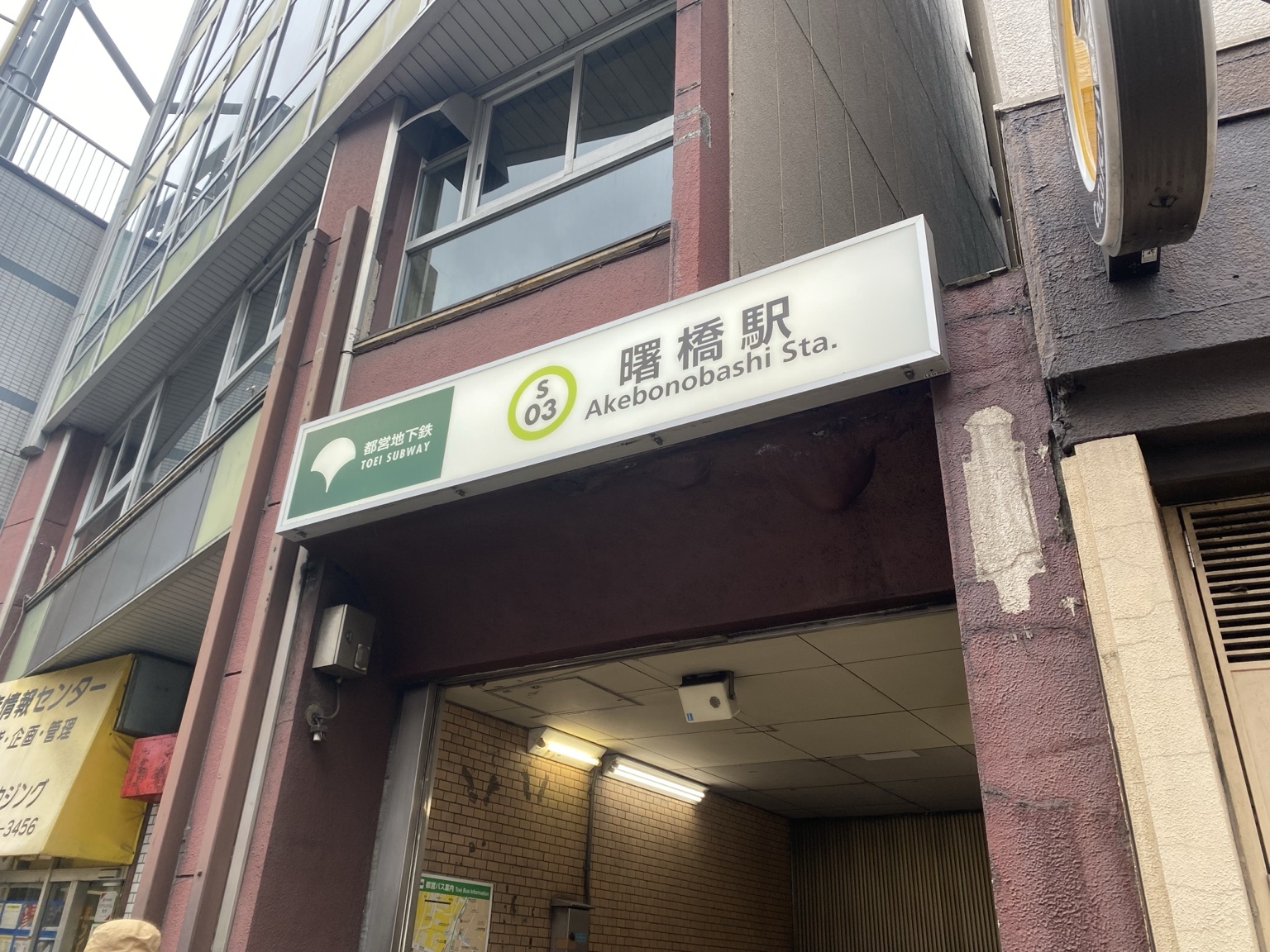 都営新宿線 曙橋駅の地上出口。赤茶色の外壁に都営地下鉄のマークとS03の駅名標