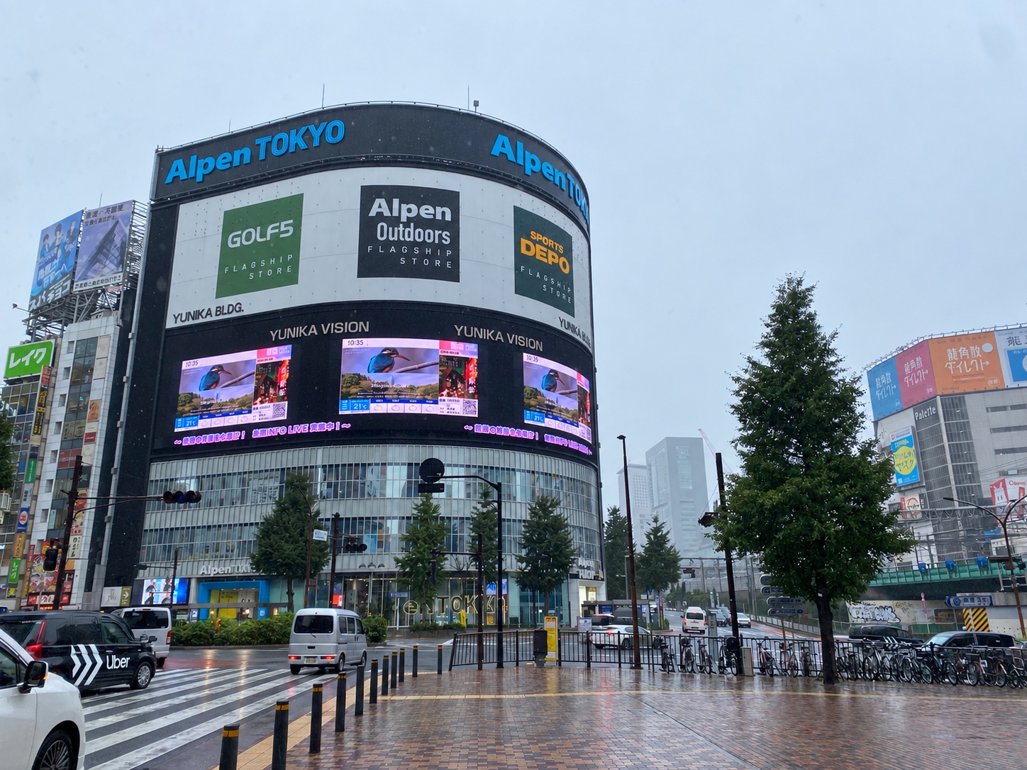 雨の日の新宿、ユニカビジョンが映るAlpen TOKYOのビル