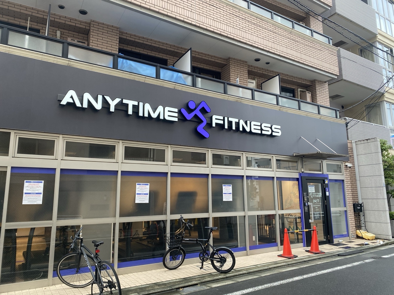 エニタイムフィットネス曙橋店の外観。マンション1階に濃紺の看板と大きなガラス窓、店の前に自転車