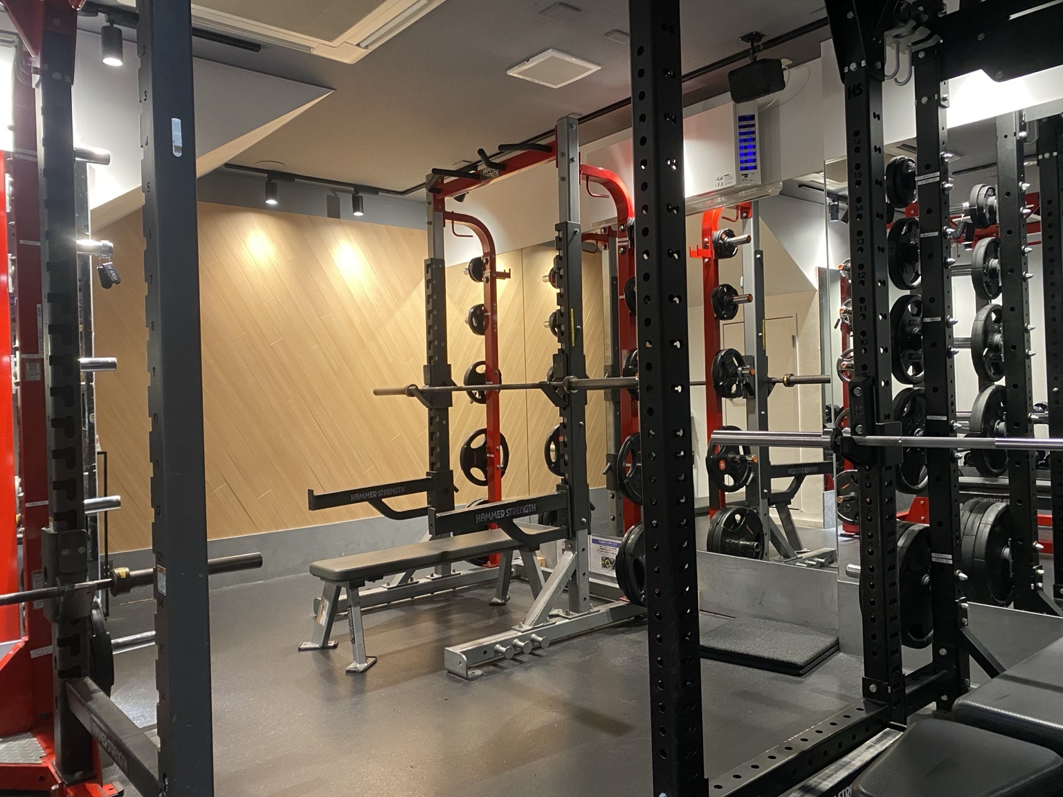 地下1階のラックエリア。黒と赤のHammer Strengthのラックが並び、木目の壁とスポットライトに照らされている