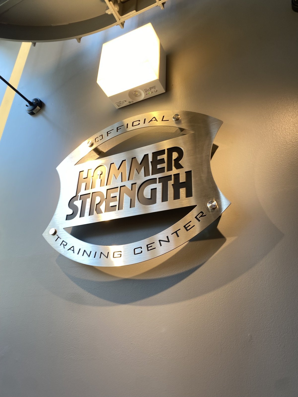 2階へ上がる階段の踊り場に掲げられた「OFFICIAL HAMMER STRENGTH TRAINING CENTER」の認定プレート